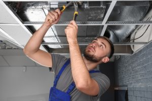 Young male technician repairing air conditioner indoors